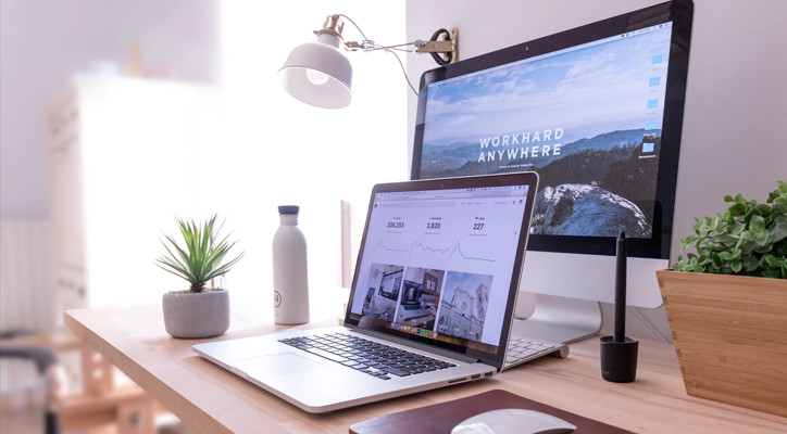 A view of a desktop featuring a computer monitor screen, laptop, lamp, and plant