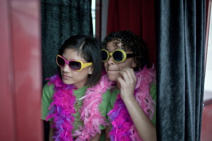 two young women in a photo booth with magenta feathers and dramatic sunglasses